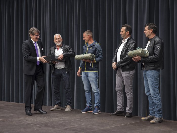 Bauarbeiterkasse der Autonomen Provinz Bozen: Ehrung der Mitglieder „30 Jahre Vertrauen“ Männer stehen auf Bühne, erhalten Geschenke bei Veranstaltung vor Vorhang