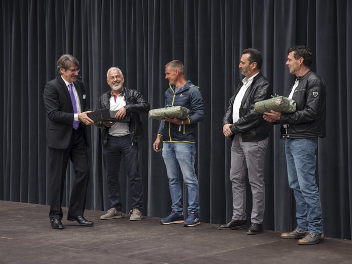 Bauarbeiterkasse der Autonomen Provinz Bozen: Ehrung der Mitglieder „30 Jahre Vertrauen“ Männer stehen auf Bühne, erhalten Geschenke bei Veranstaltung vor Vorhang