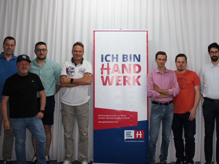 Stampa sostenibile Sette uomini in piedi accanto a uno striscione con la scritta Ich bin Handwerk