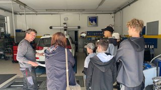 News Mechaniker erklärt einer Gruppe Jugendlicher ein Auto in der Werkstatt