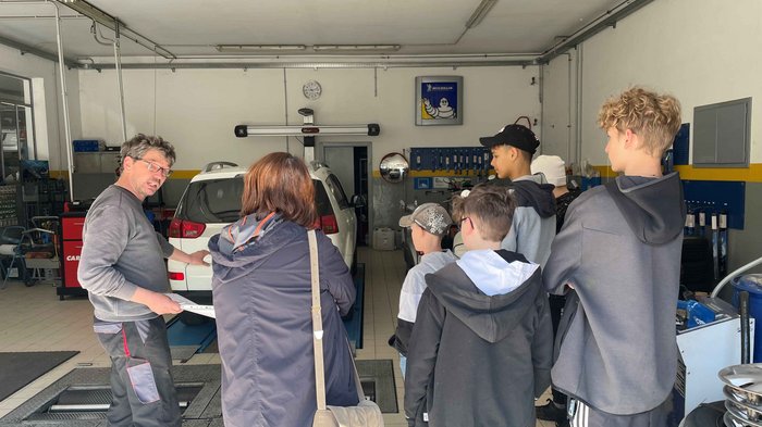 Die Jugendlichen der Mittelschule Latsch über die praktischen Berufe im Hotel- und Gastgewerbe zu informieren: das war das Ziel der Berufsinformationsveranstaltung der Junghandwerkerinnen und Junghandwerker im Wirtschaftsverband für Handwerk und Dienstlei Mechaniker erklärt einer Gruppe Jugendlicher ein Auto in der Werkstatt
