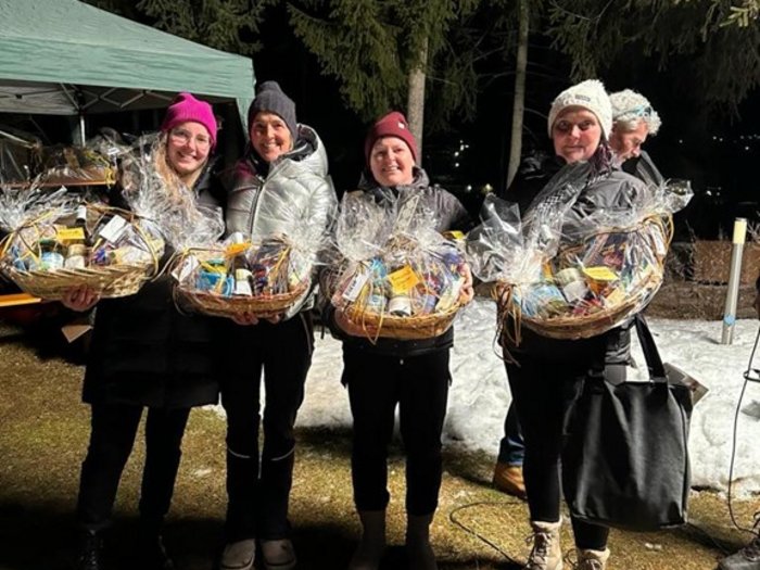 Lattlschießen der Handwerker/innen erfreut sich größter Beliebtheit Vier Frauen mit Geschenkkörben bei Nacht im Freien, Schnee im Hintergrund