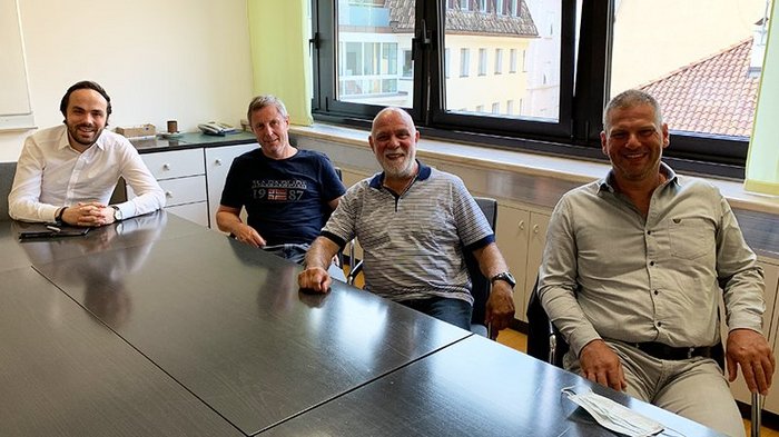 Tapezierer/Raumausstatter: Lehrzeit an Zukunft anpassen Vier Männer sitzen um einen Konferenztisch in einem Büro mit Fenster im Hintergrund.