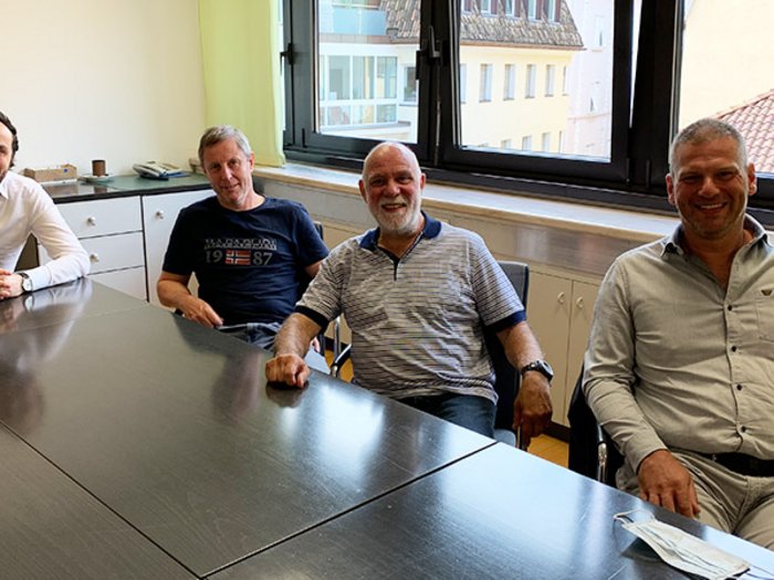 Tapezierer/Raumausstatter: Lehrzeit an Zukunft anpassen Vier Männer sitzen um einen Konferenztisch in einem Büro mit Fenster im Hintergrund.