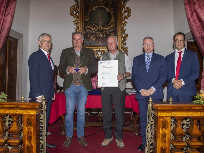 Premio Economia Alto Adige 2023: 6 aziende artigiane di lvh.apa insignite Cinque uomini in abiti formali e tradizionali ricevono un premio in una sala barocca