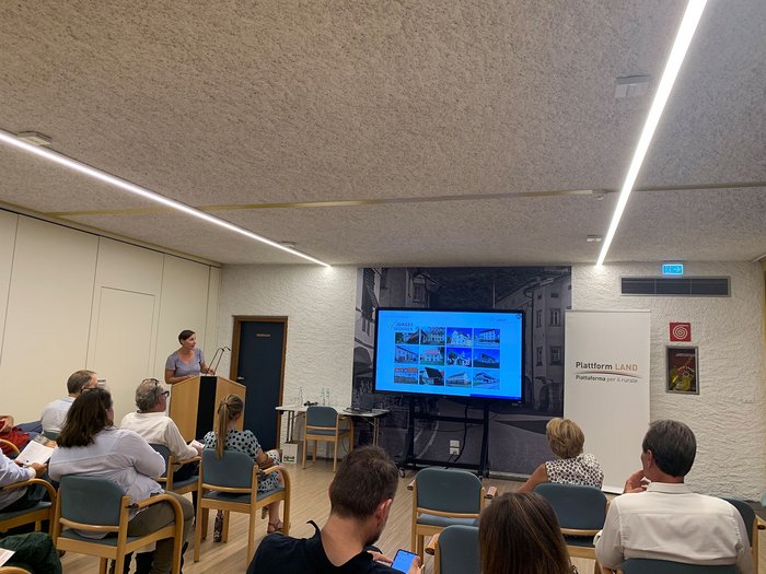 © Plattform Land Frau präsentiert Wohnprojekte vor sitzendem Publikum in einem Konferenzraum