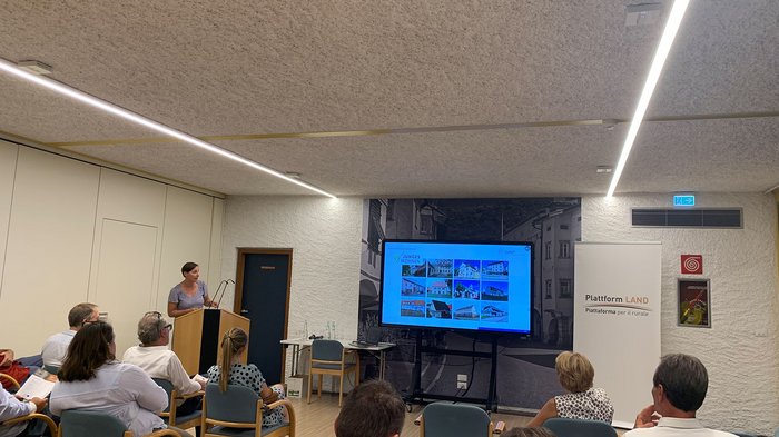 © Plattform Land Frau präsentiert Wohnprojekte vor sitzendem Publikum in einem Konferenzraum