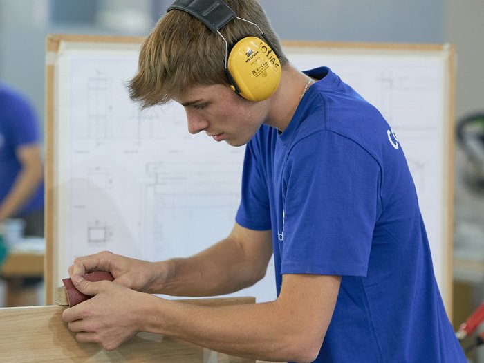 WorldSkills Italy: Obiettivo Lione Giovane uomo carteggia un pezzo di legno in laboratorio