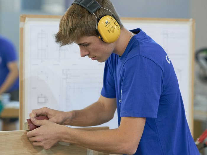 WorldSkills Italy: Lyon als Ziel Junger Mann schleift Holzstück mit Schleifpapier in Werkstatt