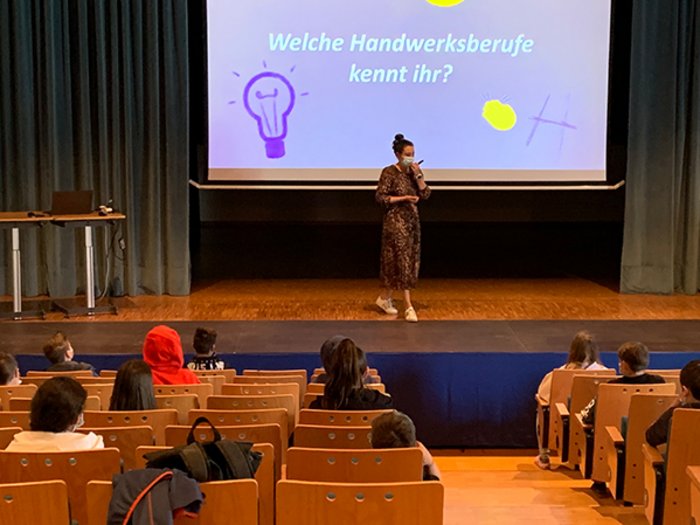 Junghandwerker und HGJ in Mals und Glurns zu Besuch Lehrerin mit Maske spricht vor Kindern in einem Hörsaal über Handwerksberufe