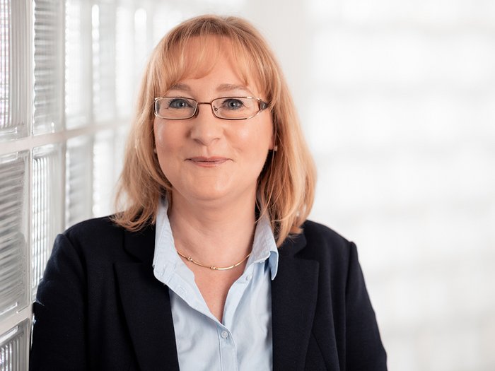 Alta Val d‘Isarco: gli artigiani guardano al futuro con fiducia e ottimismo Ritratto di donna con occhiali, camicia e giacca davanti a muro di vetro chiaro