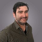 Günther Steier Ritratto di uomo sorridente con maglia scura su sfondo grigio