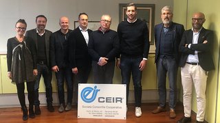 News Gruppe von acht Personen steht hinter einem CEIR Firmenschild in einem Büro