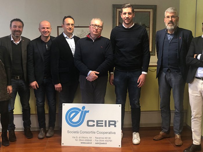 Der Austausch zwischen Konsortien ist grundlegend Gruppe von acht Personen steht hinter einem CEIR Firmenschild in einem Büro