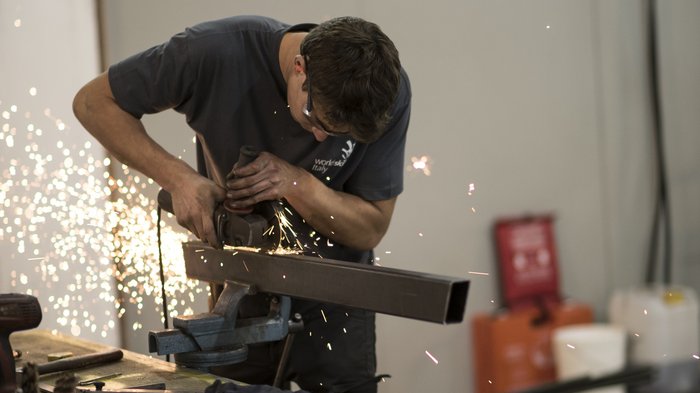 Ja zu Dienstwohnungen und Mitarbeiterunterkünften Mann schleift Metallrohr mit Winkelschleifer, Funken fliegen