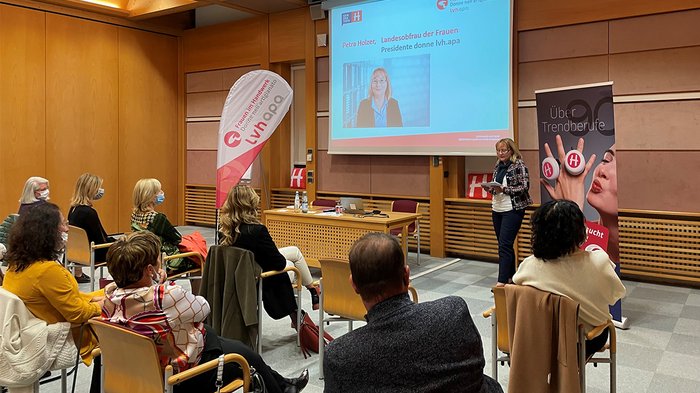 Eine geballte Ladung Frauenpower Frau hält Vortrag vor sitzendem Publikum in einem Konferenzraum