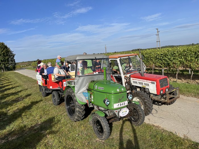 Althandwerker/innen unterwegs: Rundfahrt Weinviertel Traktorfahrt mit zwei Traktoren und Anhänger voller Menschen in einer Weinberglandschaft