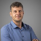 Dr. Arnold Villgrattner Uomo con camicia blu e braccia incrociate su sfondo grigio