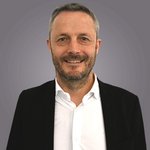 Das lvh-Team Porträt eines lächelnden Mannes mit Bart in schwarzem Sakko und weißem Hemd vor grauem Hintergrund