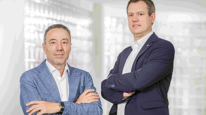 Energie- und Kubaturboni Zwei Männer in Anzügen mit verschränkten Armen vor hellem Hintergrund