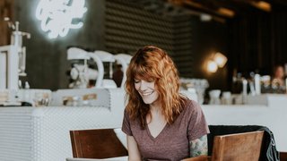 News Lächelnde Frau mit rotem Haar arbeitet mit Laptop in Kaffeehaus