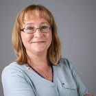 Donne nell‘artigianato Ritratto di donna sorridente con occhiali e capelli biondi su sfondo grigio