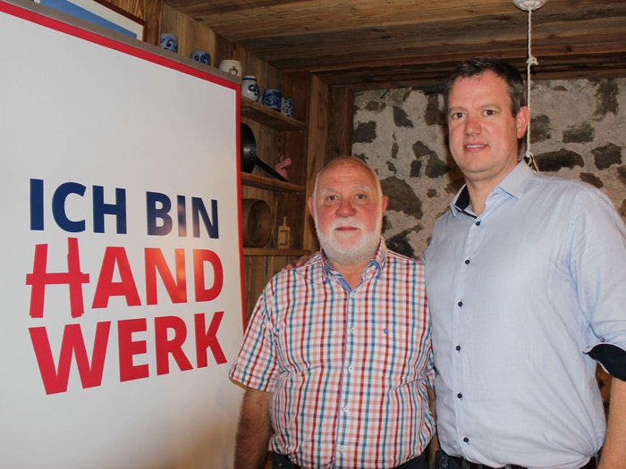 JV der Tapezierer/innen-Raumausstatter/innen Zwei Männer stehen neben einem Banner mit der Aufschrift Ich bin Handwerk