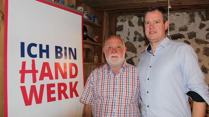 JV der Tapezierer/innen-Raumausstatter/innen Zwei Männer stehen neben einem Banner mit der Aufschrift Ich bin Handwerk