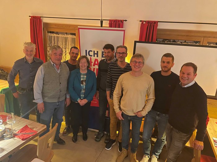 Il gruppo locale lvh.apa di Caldaro sceglie un nuovo presidente Foto di gruppo di nove persone in una stanza davanti a un poster e finestre con tende rosse