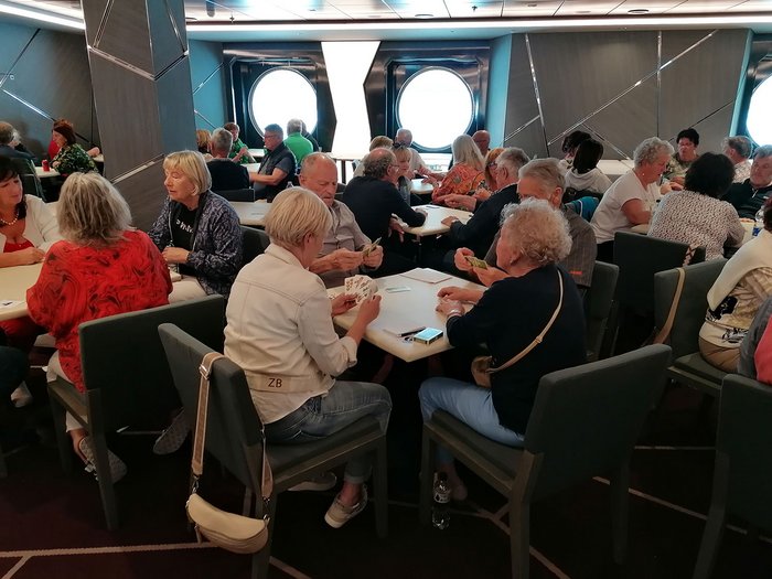 Artigiani anziani in crociera Anziani che giocano a carte a più tavoli in una stanza con oblò