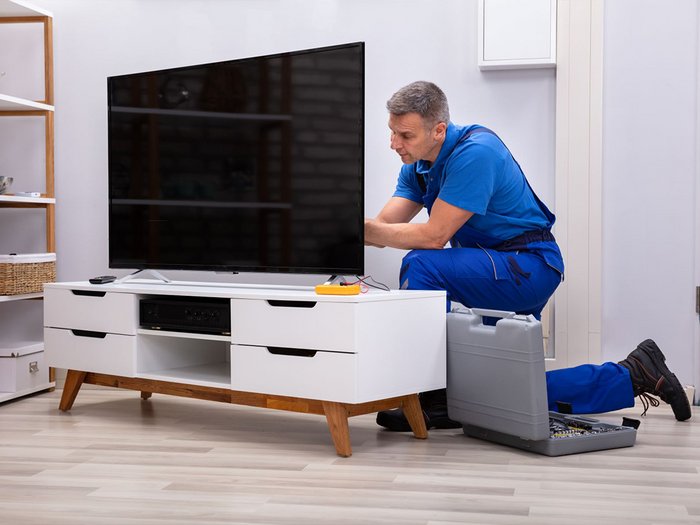Kommunikationstechniker im lvh: Jetzt Fernsehkanäle umstellen Techniker in blauer uniform repariert fernseher im wohnzimmer