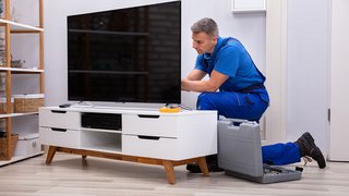 News Techniker in blauer uniform repariert fernseher im wohnzimmer