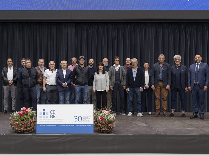 Bauarbeiterkasse der Autonomen Provinz Bozen: Ehrung der Mitglieder „30 Jahre Vertrauen“ Gruppe von 18 Personen auf Bühne mit CE BK 30 Jahre Jubiläumsschild