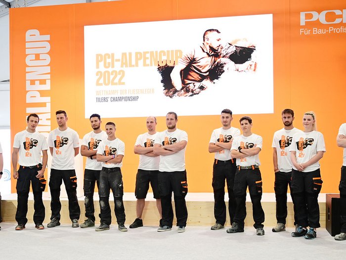 Foto 3 - Alle Teilnehmer des PCI-Alpencups 2022 © Roland Strimmer Teilnehmer des PCI Alpencups 2022 vor orangem Hintergrund und Werbetafel