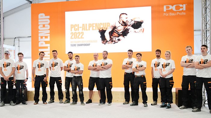 PCI-Alpencup 2022: secondo posto per i piastrellisti altoatesini! Partecipanti alla PCI Alpencup 2022 davanti a sfondo arancione e cartello pubblicitario