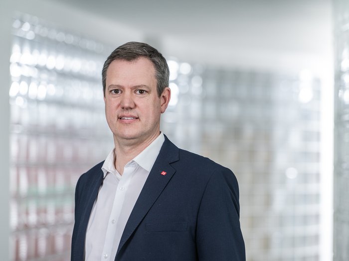 Raum für das Südtiroler Handwerk Porträt eines Mannes im Anzug vor Glassteinwand im Büro