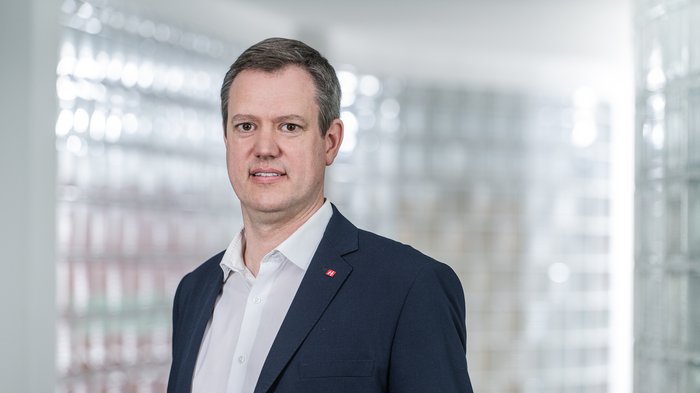 Raum für das Südtiroler Handwerk Porträt eines Mannes im Anzug vor Glassteinwand im Büro