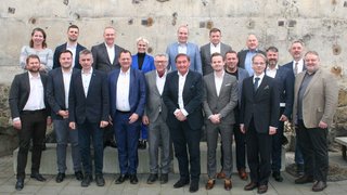 News Gruppenfoto von 19 Personen vor einer Betonwand im Freien