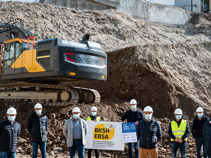 Arbeits- und Gesundheitsschutz auf Baustellen ausgebaut – Sensibilisierung verstärken Gruppe von Bauarbeitern mit Helmen und Masken vor einer Baustelle mit Bagger