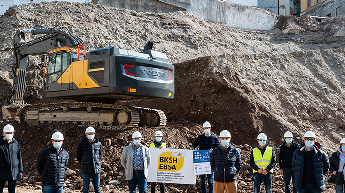 Arbeits- und Gesundheitsschutz auf Baustellen ausgebaut – Sensibilisierung verstärken Gruppe von Bauarbeitern mit Helmen und Masken vor einer Baustelle mit Bagger