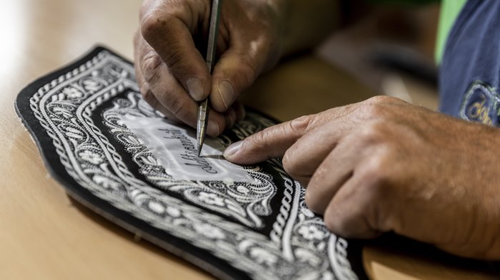 © Alan Bianchi Hände schnitzen Muster mit Werkzeug auf schwarzem Stoff