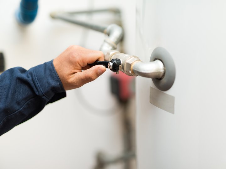 Percorso formativo Mano che apre una valvola su un tubo fissato a una parete bianca