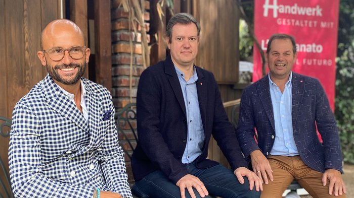 Handwerk benötigt klare Gesetze und schlanke Verfahren Drei Männer sitzen vor Holzhaus mit Banner zum Thema Handwerk und Zukunft