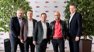 News Fünf Männer in Businesskleidung posieren vor Firmenbanner und Pflanzen