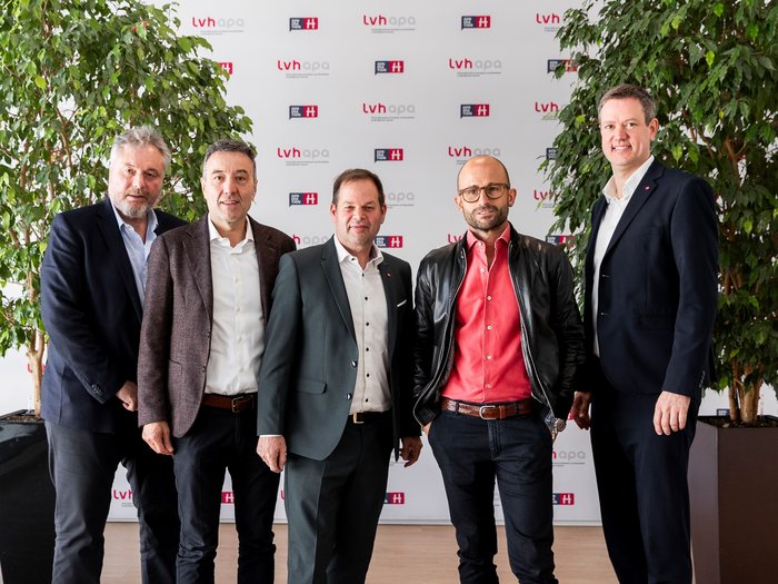 „Handwerk macht stolz“: Landesversammlung des Südtiroler Handwerks feiert Leistungen, Menschen und Visionen Fünf Männer in Businesskleidung posieren vor Firmenbanner und Pflanzen