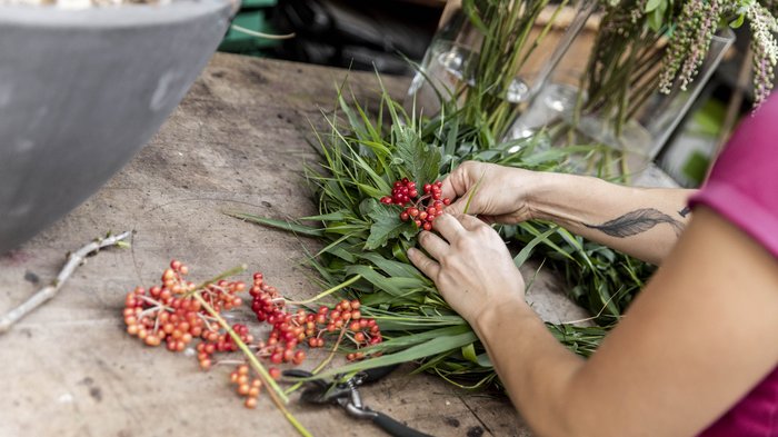 © Alan Bianchi Person arrangiert rote Beeren und Grünpflanzen auf einem Holztisch