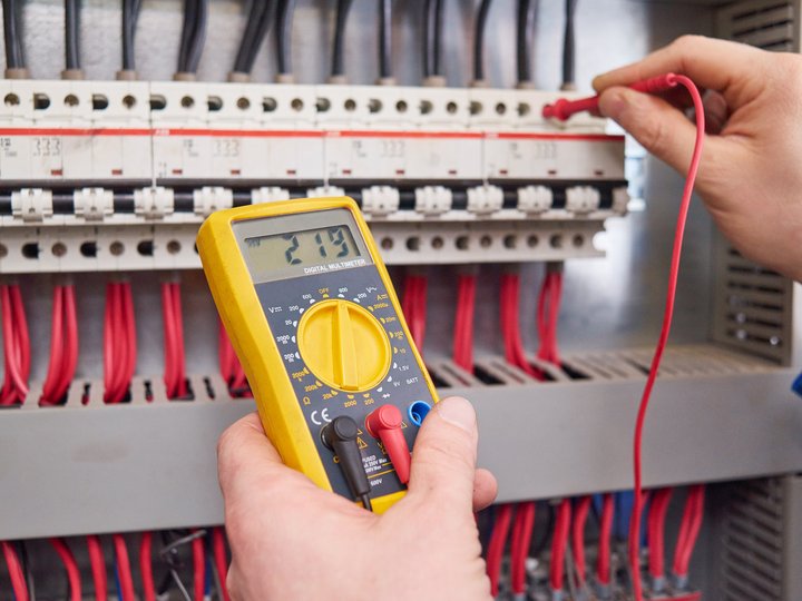 Elettrotecnici Persona misura la tensione con multimetro digitale in un quadro elettrico