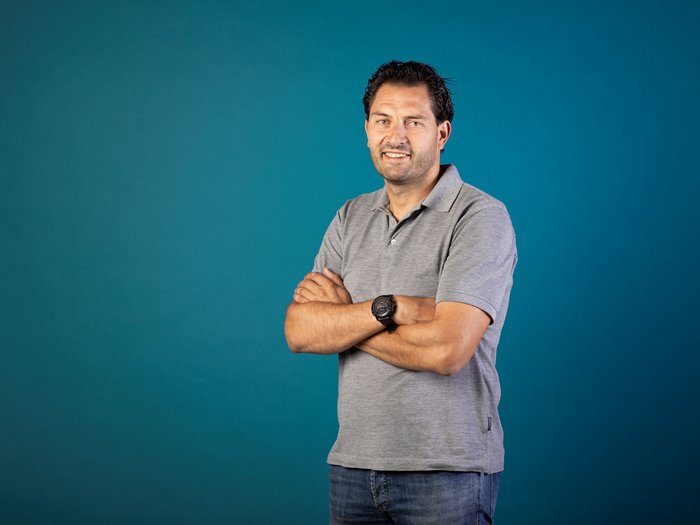 „Eine starke Interessenvertretung erfordert eine aktive Beteiligung aller“ Mann in grauem Polohemd steht vor blauem Hintergrund mit verschränkten Armen