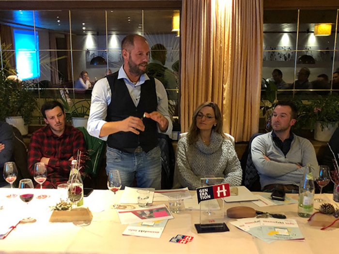 Handwerk im Gemeinderat Sechs Personen sitzen an einem Tisch, eine spricht, Weingläser und Dokumente liegen auf dem Tisch