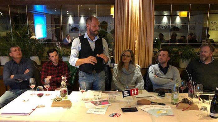Handwerk im Gemeinderat Sechs Personen sitzen an einem Tisch, eine spricht, Weingläser und Dokumente liegen auf dem Tisch